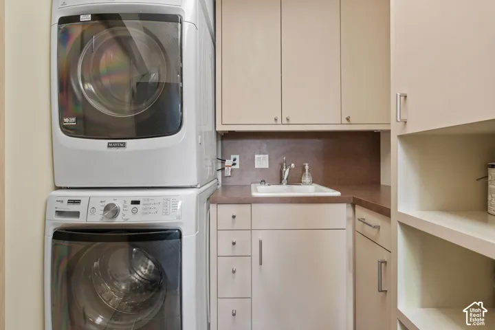 Laundry area featuring stacked appliances, built-in cabinetry, a drop-in sink with a chrome faucet, and integrated open shelving
