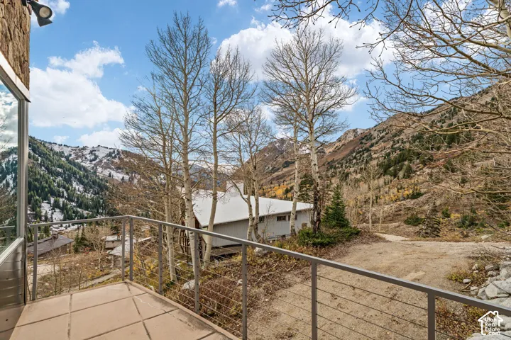 Outdoor balcony with metal cable railing, paved flooring, stone exterior wall detailing, and mountain backdrop