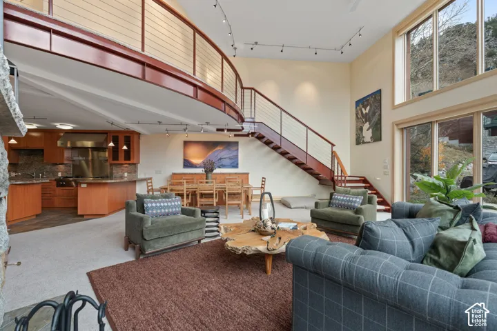 Double-height ceiling, curved mezzanine with cable railing, expansive floor-to-ceiling windows, natural stone fireplace surround, and wood cabinetry with stainless steel integrated appliances