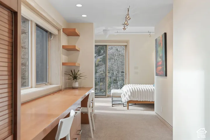 Built-in wooden desk featuring integrated storage and floating shelving, recessed ceiling lighting, track lighting, and sliding glass doors
