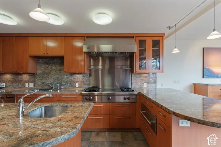 Kitchen featuring wood cabinetry, stone countertops, stainless steel professional-grade range with matching backsplash, and island with a stainless steel undermount sink