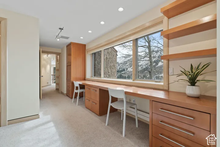 Built-in wood cabinetry, expansive wooden desk surface, multi-level floating shelving, recessed lighting, and large windows with mountain scenery