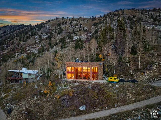 Contemporary structure featuring natural stone cladding, expansive floor-to-ceiling windows, and a flat roofline, set against a mountainous landscape with mature coniferous and deciduous trees