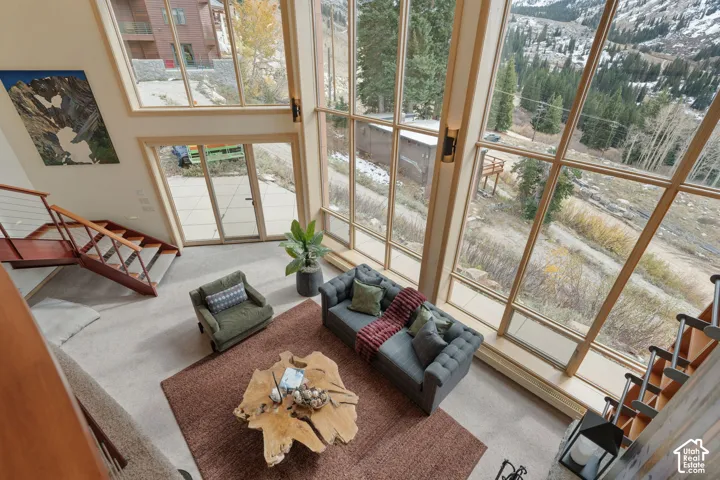 Double-height floor-to-ceiling windows, open-tread staircase with metal cable railings, and multi-panel glass door