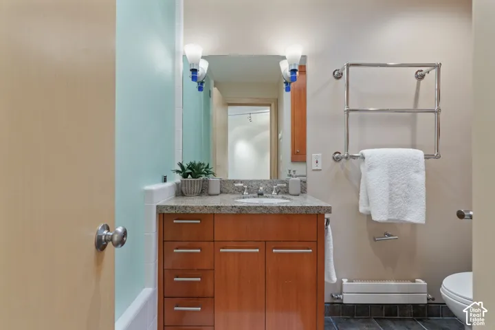 Bathroom vanity featuring a wood-finish cabinet, stone-finish countertop with an integrated undermount sink, wall-mounted light fixtures, and a polished metal towel rack