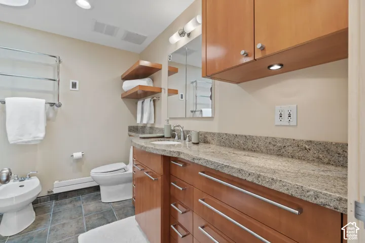 Bathroom featuring wood-finish cabinetry, stone countertop, dual-purpose bidet and toilet fixtures, floating wall shelving, and tile flooring