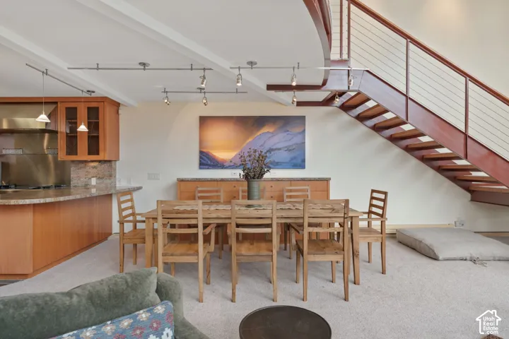 Open-concept interior featuring a custom metal staircase with cable railing, track lighting, built-in cabinetry, and integrated kitchen stone-surfaced countertops