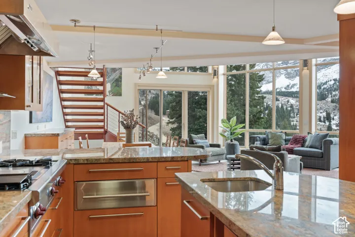 Kitchen featuring wood cabinetry, stone countertops, stainless steel appliances, tiered wooden staircase, and floor-to-ceiling windows with mountain scenery