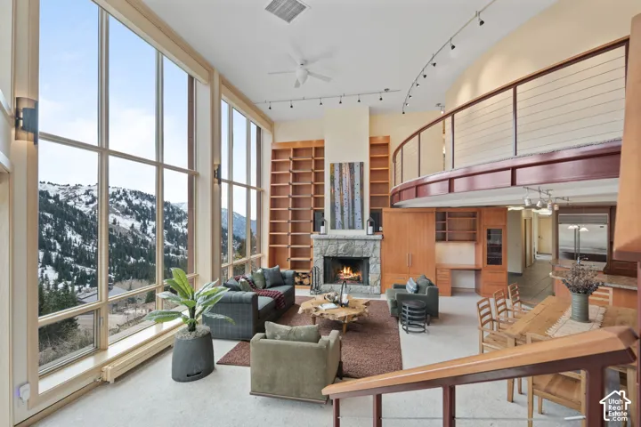 Floor-to-ceiling windows, stone-faced fireplace, built-in floor-to-ceiling wooden shelving, mezzanine level with metal railing, and track lighting