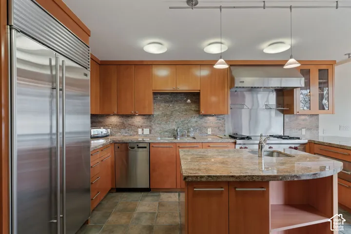 Kitchen featuring cabinetry with a wood finish, stone countertops, a stainless steel side-by-side refrigerator, a stainless steel dishwasher, and a stone tile floor