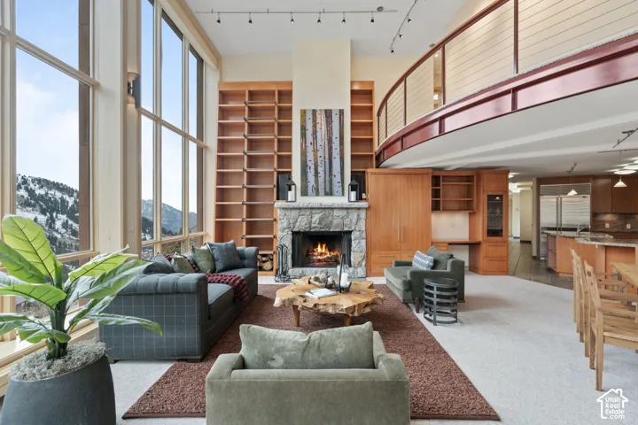 Double-height living area with floor-to-ceiling windows, stone-surround fireplace, extensive built-in wood shelving, and a curved mezzanine railing