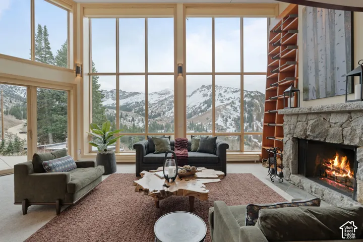 Floor-to-ceiling windows, stone fireplace with a thick mantle, built-in wooden shelving, and mountain backdrop