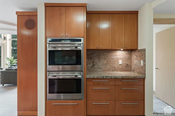 Custom wood cabinetry, stainless steel double wall ovens, stone countertops, and integrated backsplash
