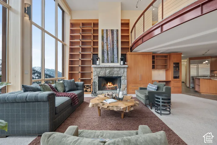 Floor-to-ceiling windows, stone-faced fireplace with floor-to-ceiling wood shelving, custom wood cabinetry, and a curved mezzanine level with a metal railing