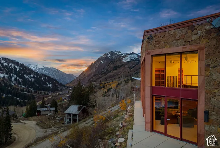 Exterior facade featuring natural stone masonry, multi-level floor-to-ceiling glass paneling, and a paved walkway, set against a mountain backdrop