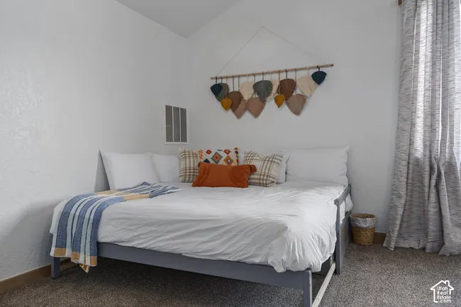 White painted walls with sloped ceiling, grey carpet flooring, and full-length curtains