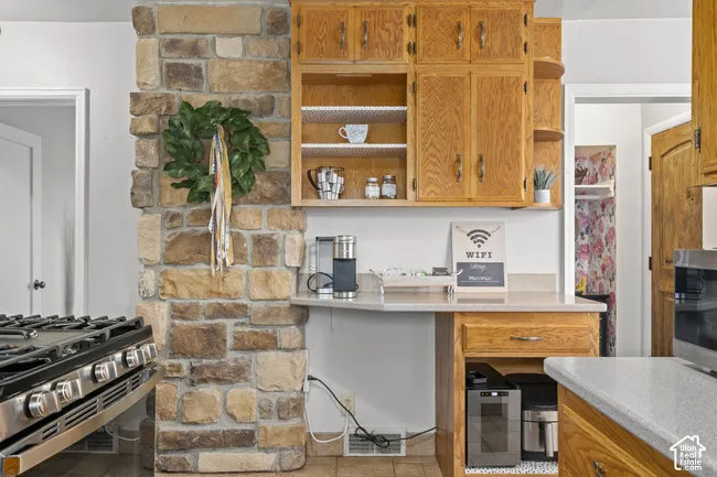 Stone-clad architectural element, light wood-finish cabinetry, light-toned countertop, and stainless steel range