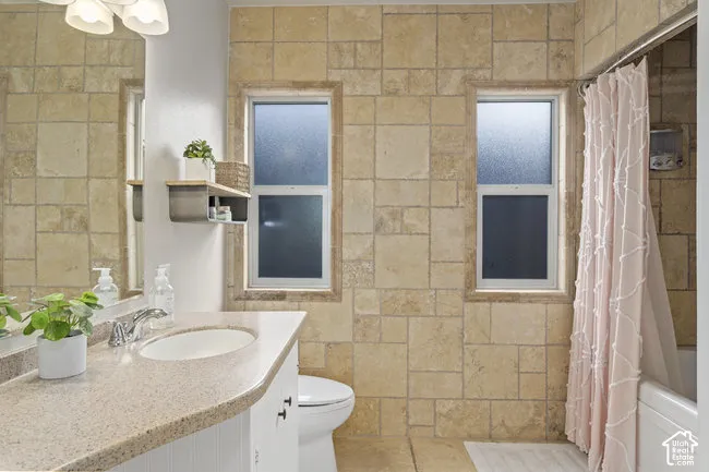 Tiled bathroom featuring a built-in bathtub, a single vanity with an integrated sink, and two frosted windows
