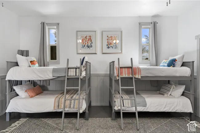 Bright shared bedroom featuring two full bunk bed units with sturdy metal frames, crisp white bedding, and ample natural light from dual tall windows with gray curtain panels