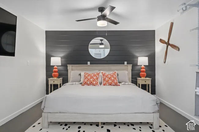 Shiplap accent wall, wood-finish flooring, ceiling fan with integrated lighting, wall-mounted television, and a wood-finish bed frame
