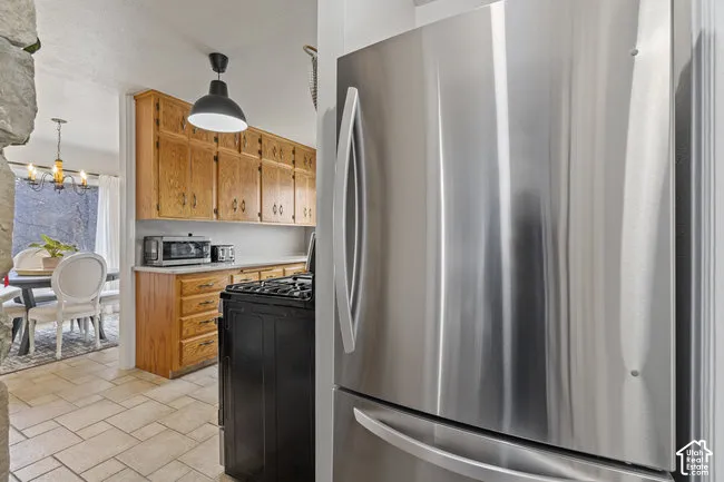 Stainless steel refrigerator, wood cabinetry, built-in range, pendant lighting, and tiled flooring