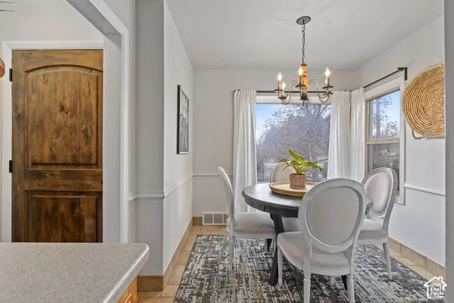 Dining area with tile flooring, chair rail molding, and a chandelier with a candelabra design