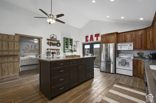 Vaulted ceiling with a ceiling fan, wood-finish flooring, central island with storage, wood cabinetry, and stainless steel appliances