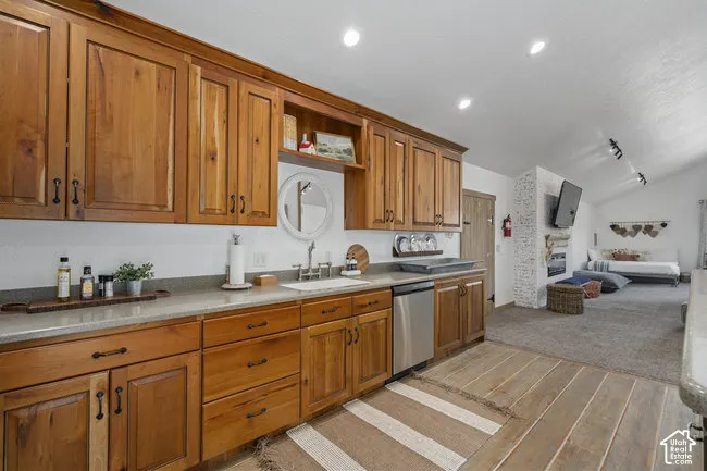 Wood cabinetry, solid surface countertops, stainless steel dishwasher, vaulted ceiling, and recessed lighting
