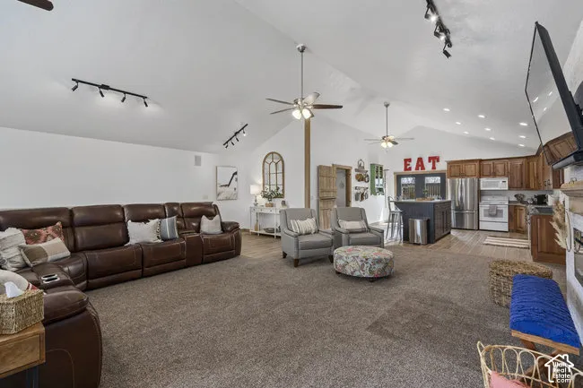 Vaulted ceilings with ceiling fans, track lighting, wood-finish flooring in kitchen area, wood cabinetry, and stainless steel appliances