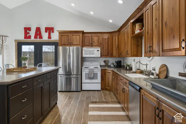 Vaulted ceiling kitchen featuring wood-finish flooring, recessed lighting, and a stainless steel refrigerator