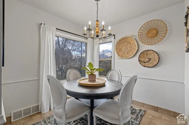 Bright dining area featuring a candelabra-style chandelier, large windows with exterior scenery, crown molding, and tiled flooring