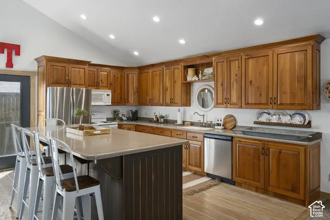 Warm wood cabinetry throughout this chef's kitchen, featuring stainless steel appliances, a spacious center island with seating, recessed lighting, and wood-finish flooring