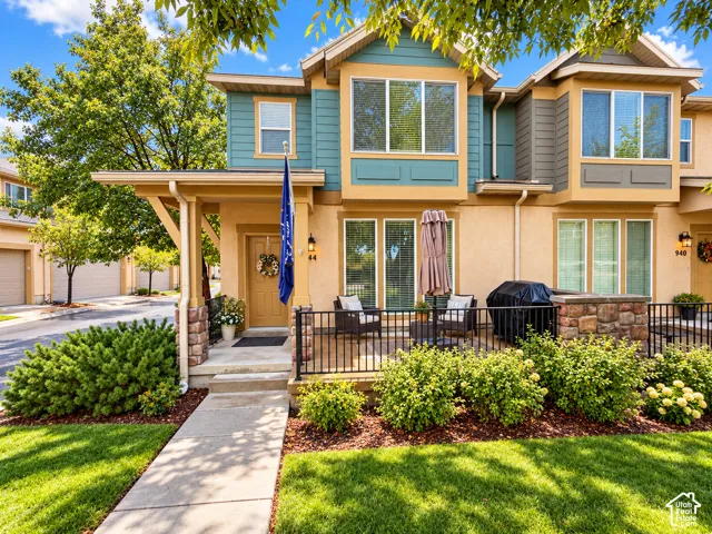 Multi-level exterior featuring stucco and horizontal siding, stone-accented front porch columns, black metal railing, concrete entry path, and mature landscape plantings
