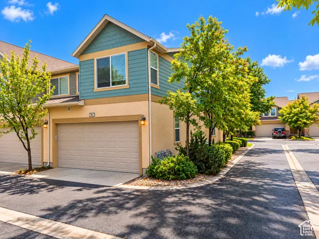 Multi-level exterior featuring a combination of shake and stucco siding, a two-car garage with an overhead door, and exterior wall-mounted lighting