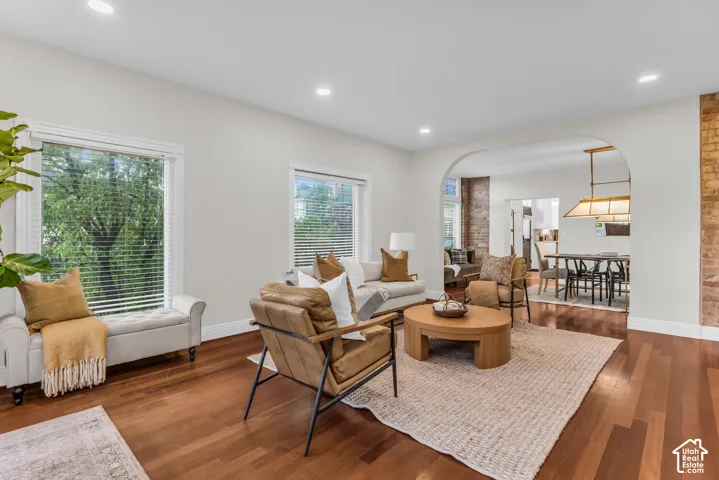 Living area featuring wood-finish flooring, recessed lighting, expansive windows, exposed brick accent wall, and a large arched entryway
