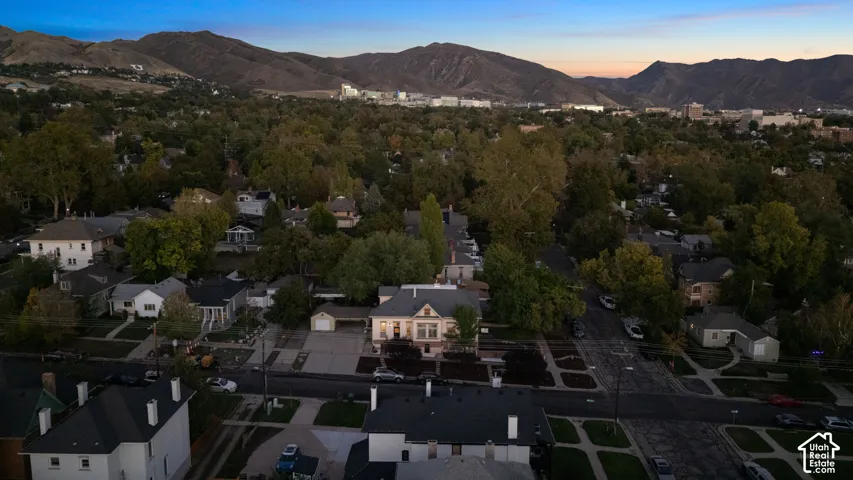 Aerial perspective featuring a multi-story residence with a detached garage, established tree canopy, and mountain backdrop
