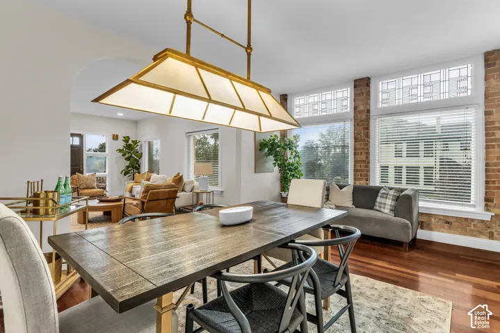 Dining space featuring wood-finish flooring, exposed brick walls, an arched entryway, transom windows, and a tiered metal chandelier