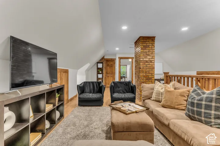 Vaulted ceilings, exposed brick column, recessed lighting, wood-finish flooring, and wooden handrail with balusters
