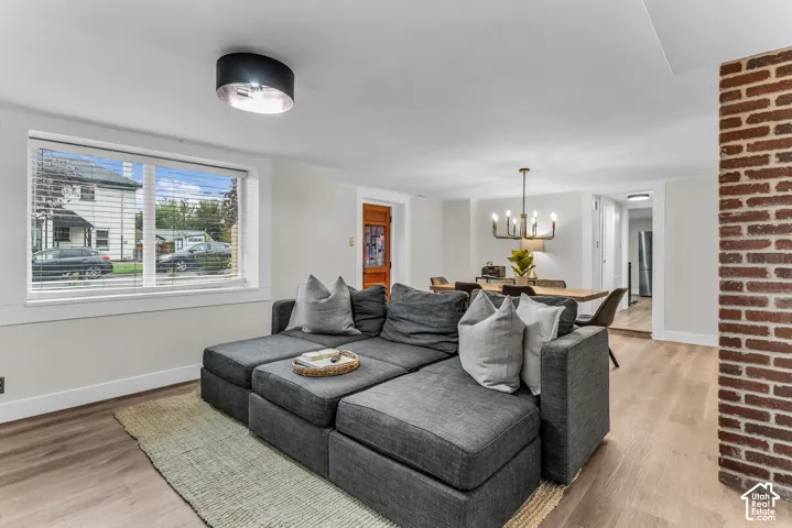 Living area featuring wood-finish flooring, exposed brick accent wall, modern drum-style flush mount lighting, and multi-light chandelier fixture
