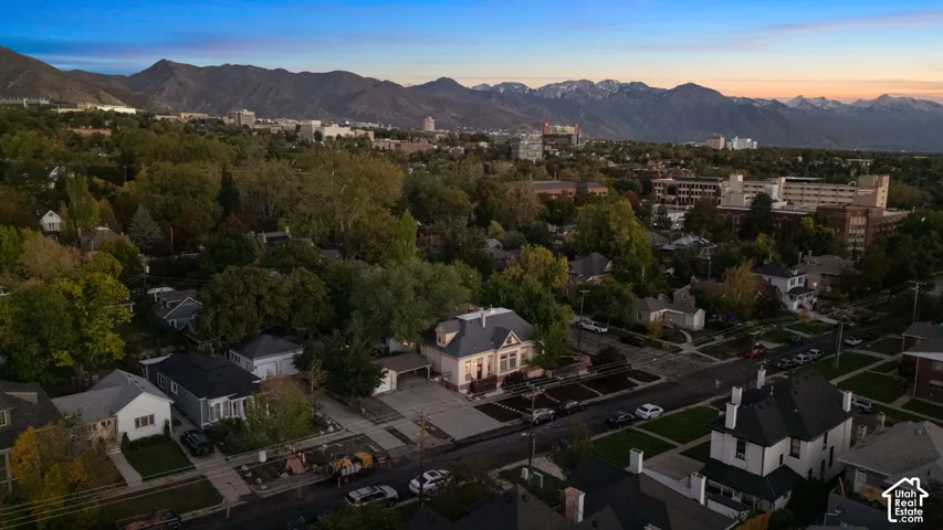 Aerial perspective of the property featuring a structured roofline, concrete driveway, attached garage, and mature trees against a mountain backdrop