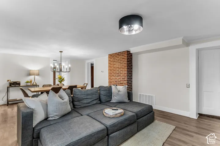 Exposed brick masonry feature, wood-finish flooring, modern drum-style flush mount lighting, and multi-arm chandelier