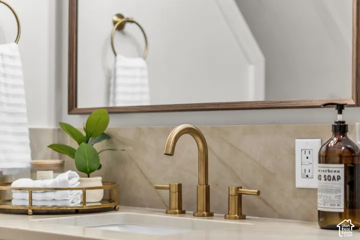 Stone-finish countertop featuring an integrated rectangular basin, brass widespread faucet, matching circular towel ring, and a coordinating framed mirror