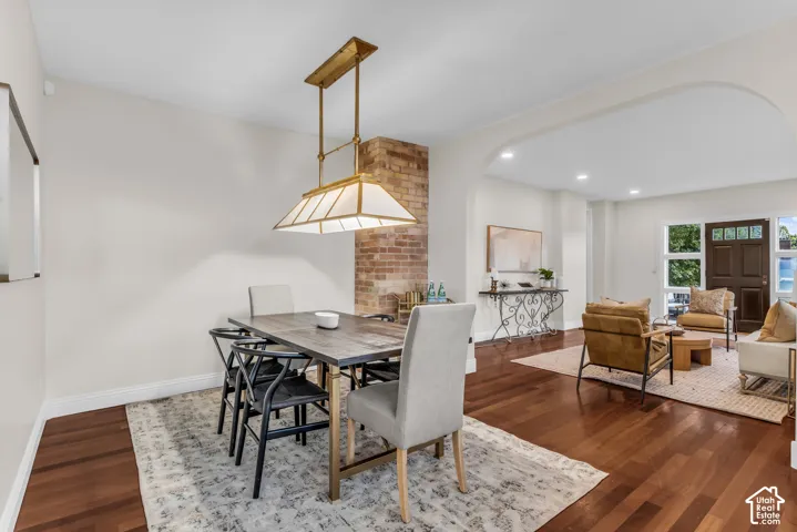 Dining area featuring wood-finish flooring, a brick chimney breast, a custom metal-frame pendant light, and a grand arched entryway