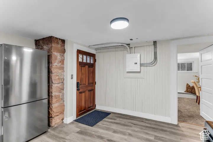 Exposed stone pillar, wood-finish flooring, paneled wall detailing, and a solid wood exterior door with glass pane accents
