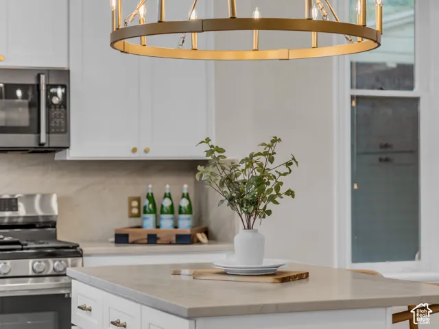 Kitchen island featuring a solid-surface countertop and white cabinetry, complemented by a large circular metal chandelier, stainless steel oven, and stone-finished backsplash