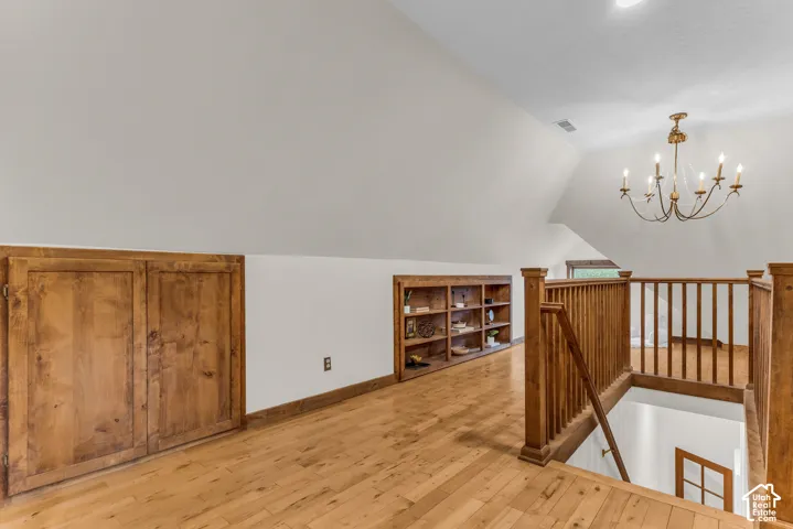 Landing featuring wood-finish flooring, built-in wooden cabinetry, recessed wall shelving, decorative chandelier, and a wood-slat railing