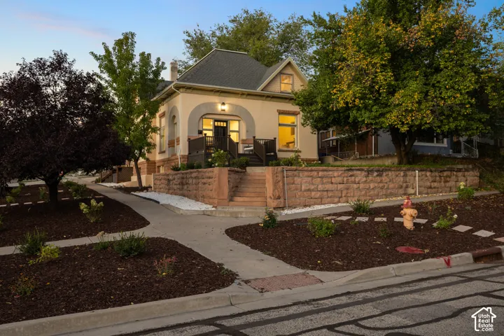 Stucco exterior featuring arched masonry detailing, a stone retaining wall, an elevated front porch with railings, and a multi-gabled roofline