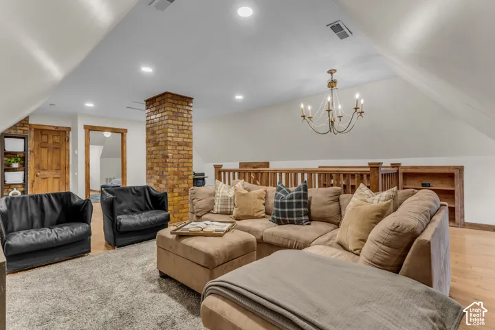 Vaulted ceiling with recessed lighting, exposed brick pillar, custom wood-trim door frames, built-in shelving, and a decorative chandelier
