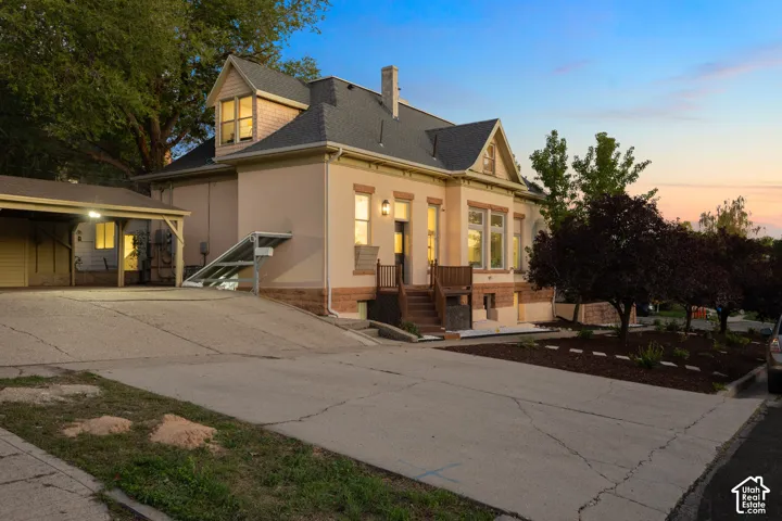 Two-story exterior featuring a stone foundation, stucco siding, a shingled roof, a covered carport, and wood-railed entry steps