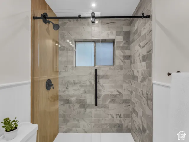 Walk-in shower featuring a sliding glass door with matte black hardware, stone-finish tile surround, and matte black plumbing fixtures